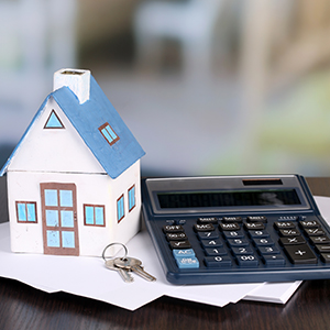 Paper house atop a stack of paper, keys, and a calculator